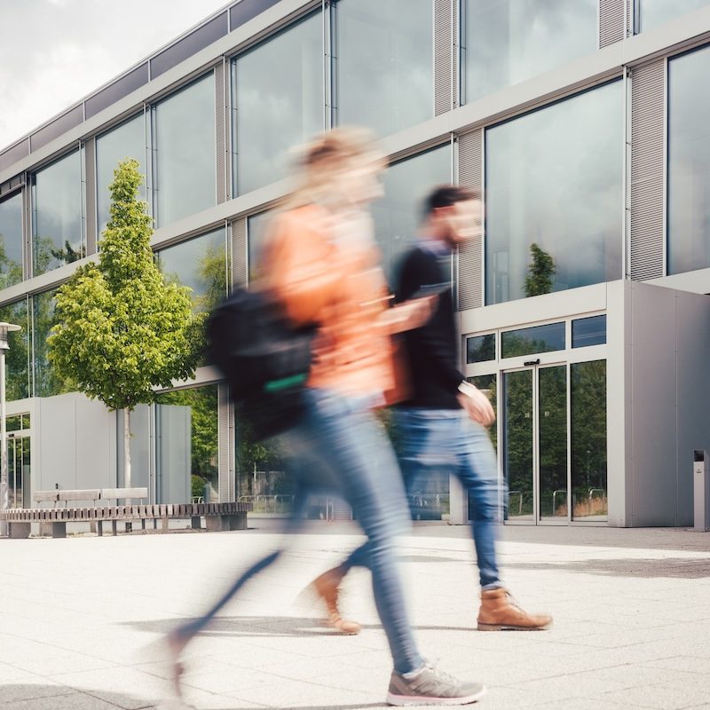 Blurred silhouette of students being busy on university campus in front of main building